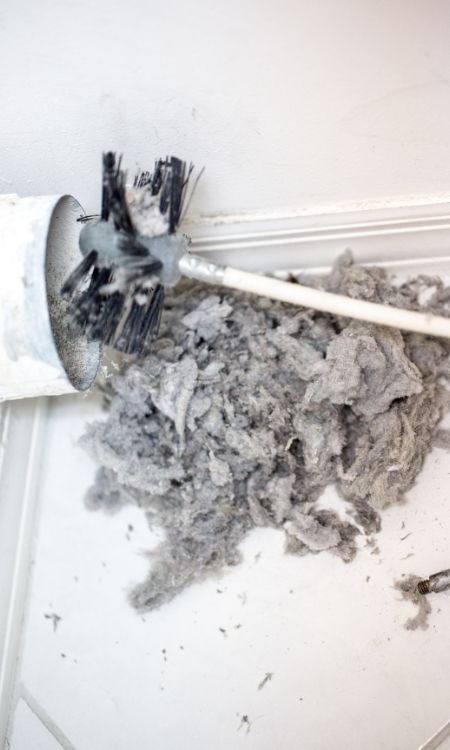 Lint being removed with a brush from a dryer vent